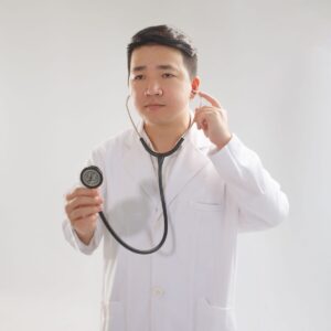 Portrait of a young doctor in white coat holding a stethoscope in a studio setting.