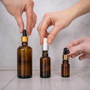 A trio of hands holding different sized essential oil dropper bottles indoors.