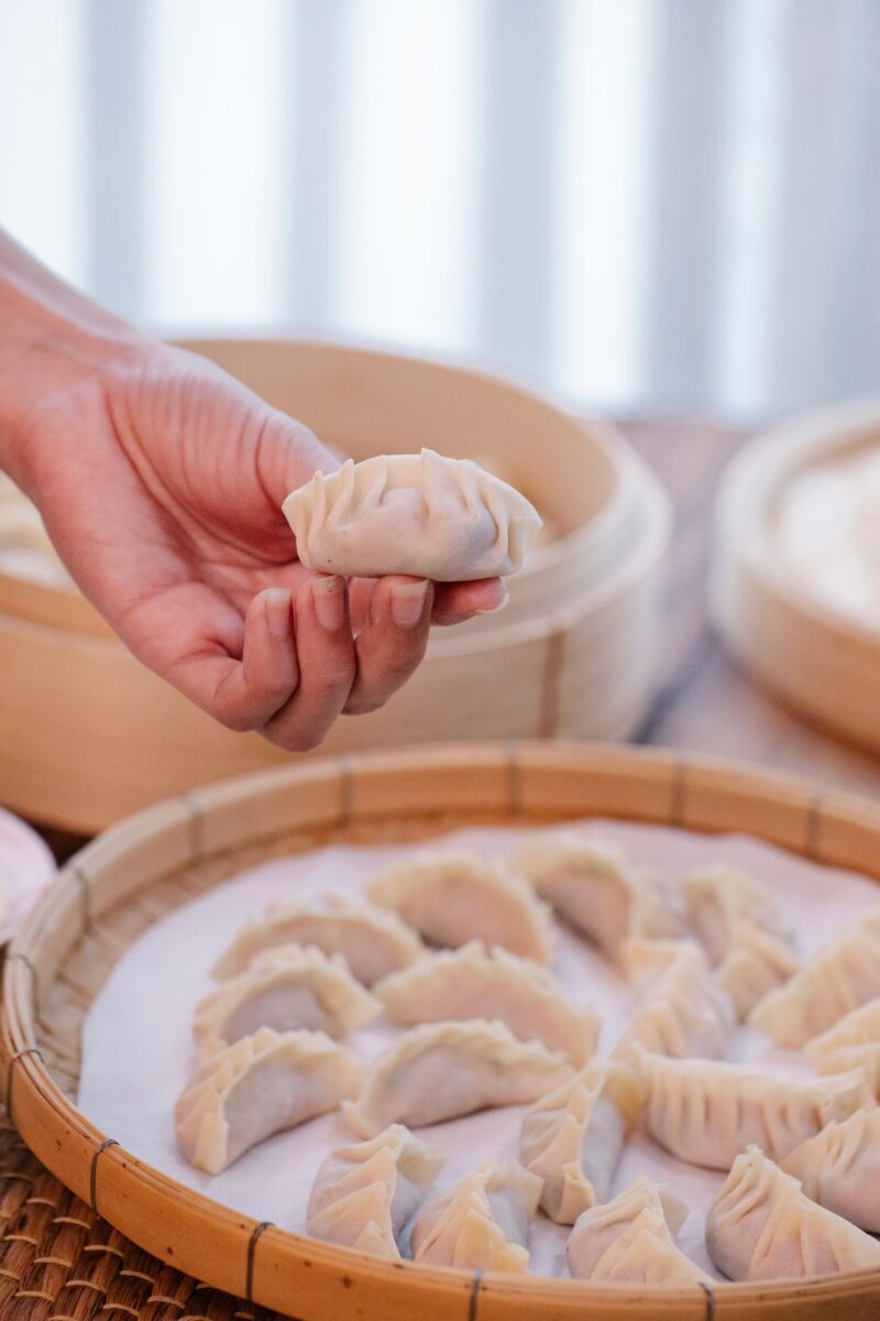 Unrecognizable crop person taking and showing delicious dumplings arranged in bamboo steamer on blurred background