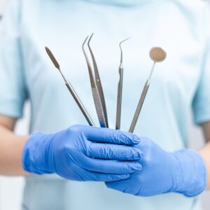 A dentist holding various dental tools in gloved hands, ready for use.